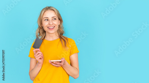 Dreamy woman holding bank card and smartphone with online app