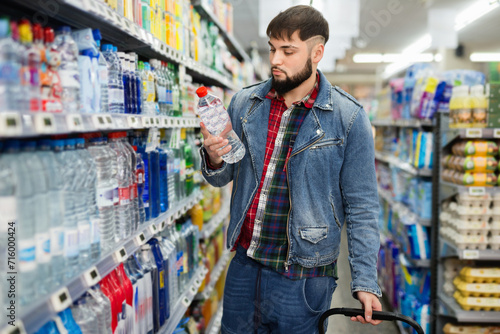 Portrait of focused young glad cheerful positive man purchasing bottled water in grocery store photo