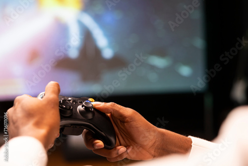 Close up shot of controller held by man playing galaxy flying videogame on smart TV, relaxing. Competitive gamer using joystick to have fun on gaming console in stylish apartment living room