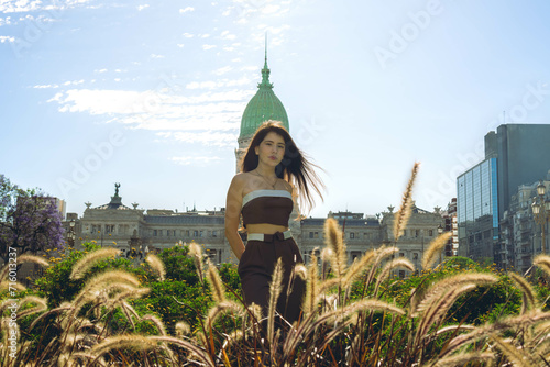 Young Latin woman tourist looks at the camera on a sunny day in buenos aires, with the argentine national congress in the background