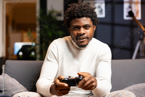 Happy man playing shooter videogame in warm apartment, holding controller. Gamer participating in online multiplayer game using gaming system, spamming buttons on gamepad