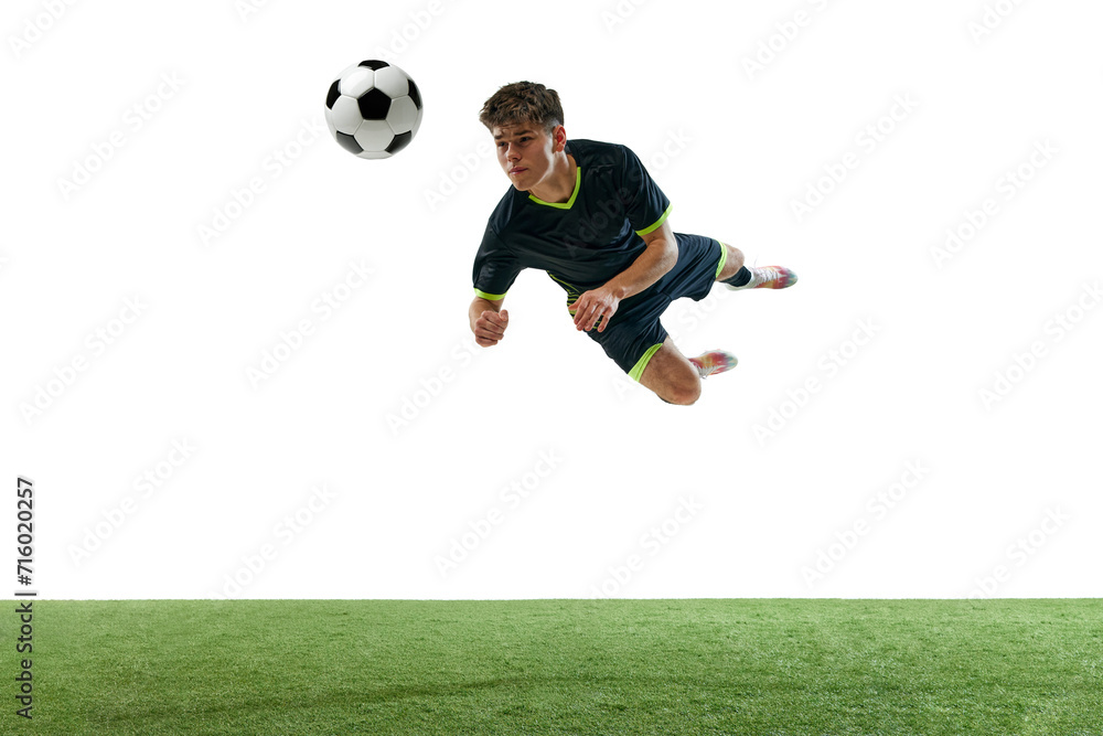 Dynamic image of young man, football player in motion, hitting ball with head isolated over white background with grass flooring. Concept of sport, game, competition, championship, active lifestyle