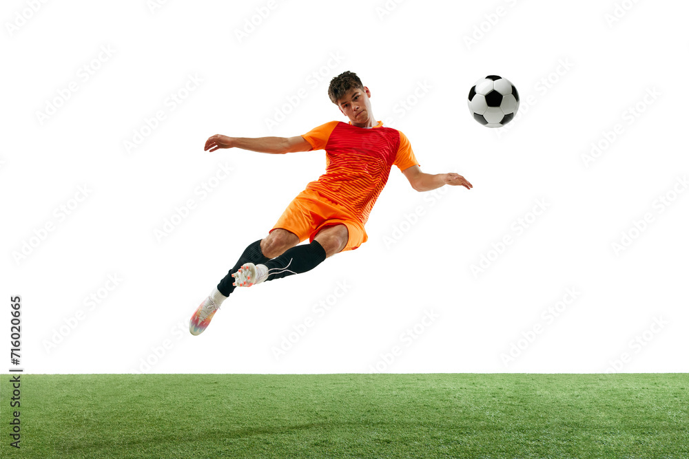Dynamic image of competitive young man in orange uniform training, hitting ball in a jump isolated over white background with grass flooring. Concept of sport, game, competition, active lifestyle