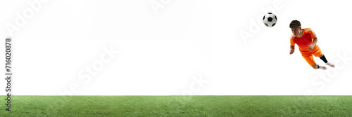 Young man  football player in orange hitting ball in a jump with head isolated over white background with grass flooring. Concept of sport  game  competition  championship  active lifestyle. Banner
