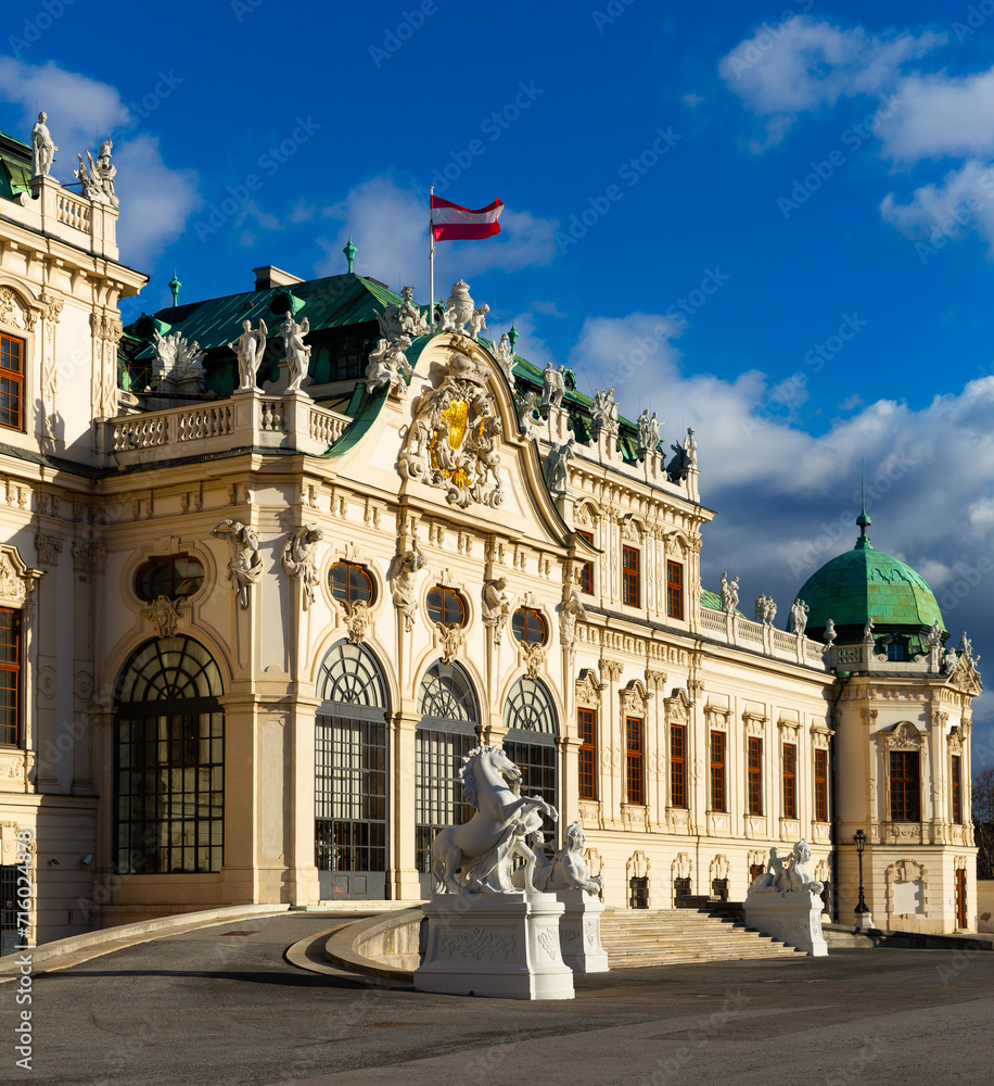 Scenic view of main facade and entrance of baroque building of upper Belvedere palace with large staircase and various sculptures on sunny day, Vienna, Austria