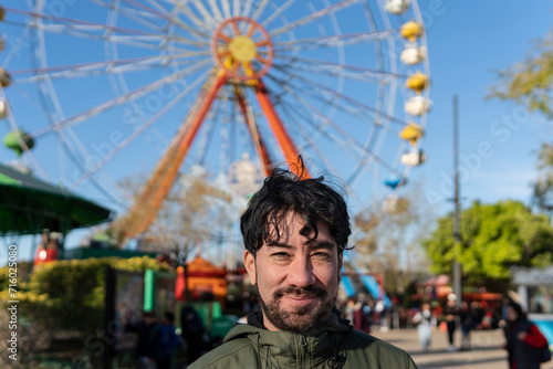 Portrait of latino man in an amusement park posing happy with the ferris wheel in the background