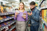 Young cheerful couple shopping together in grocery, choosing tasty chocolate