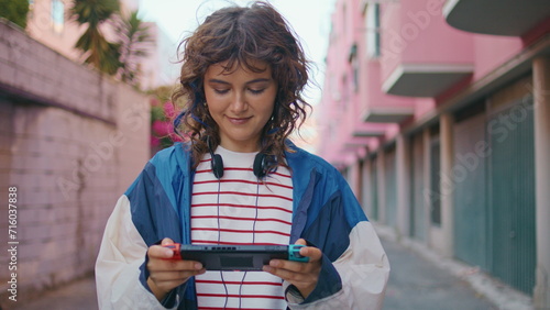Teenager playing handheld console walking urban area. Woman focused on display  © stockbusters