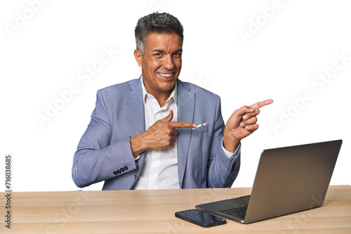 Elegant businessman at desk with laptop excited pointing with forefingers away.