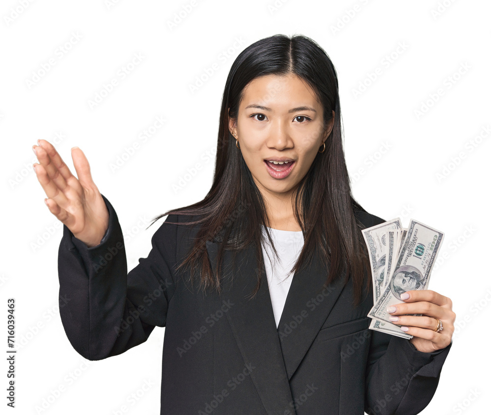 Young Chinese woman with dollars in suit receiving a pleasant surprise, excited and raising hands. Young Chinese woman with dollars in suit receiving a pleasant surprise, excited and raising hands.