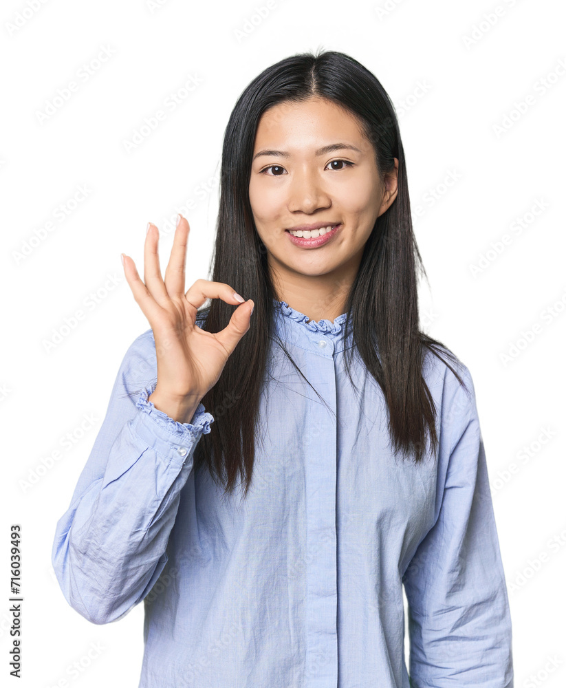 Young Chinese woman in blue shirt cheerful and confident showing ok gesture. Young Chinese woman in blue shirt cheerful and confident showing ok gesture.