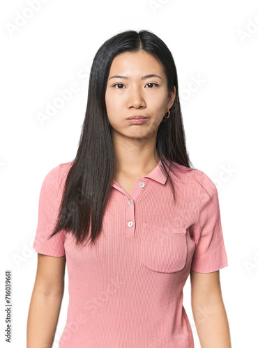 Young Chinese woman in studio setting blows cheeks, has tired expression. Facial expression concept. © Asier