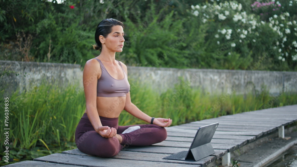 Calm lady sitting lotus position park bench. Woman watching online yoga lesson