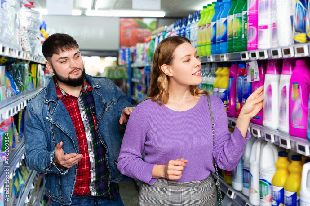 Portrait of positive glad pleasant beautiful woman and man choosing liquid laundry detergents during shopping at supermarket