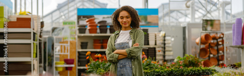 Smiling female garden shop seller standing with crossed hands on flower store background photo