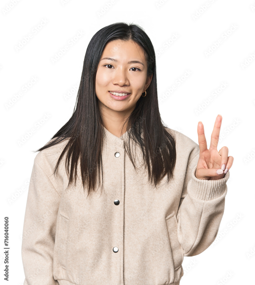 Young Chinese woman in studio setting showing victory sign and smiling broadly. Young Chinese woman in studio setting showing victory sign and smiling broadly.