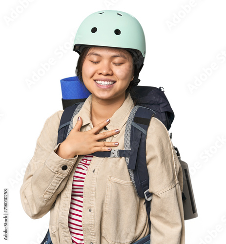 Chinese woman geared up for mountain activities laughs out loudly keeping hand on chest. © Asier