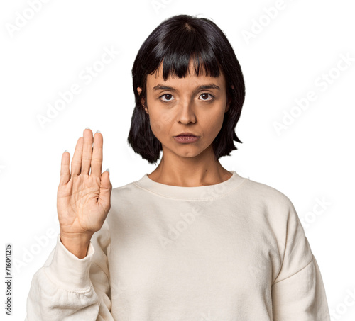 Young Hispanic woman with short black hair in studio standing with outstretched hand showing stop sign, preventing you.