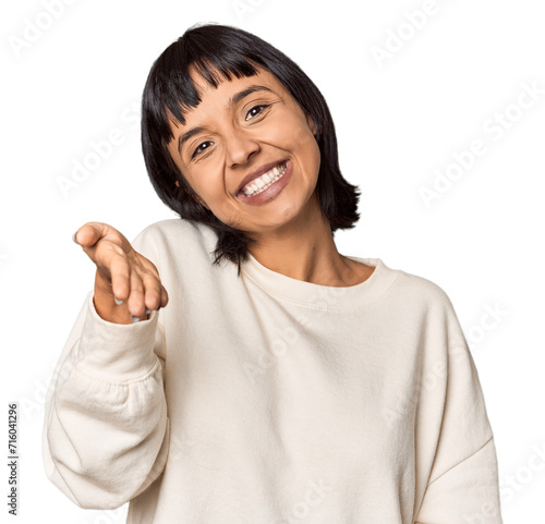 Young Hispanic woman with short black hair in studio stretching hand at camera in greeting gesture.