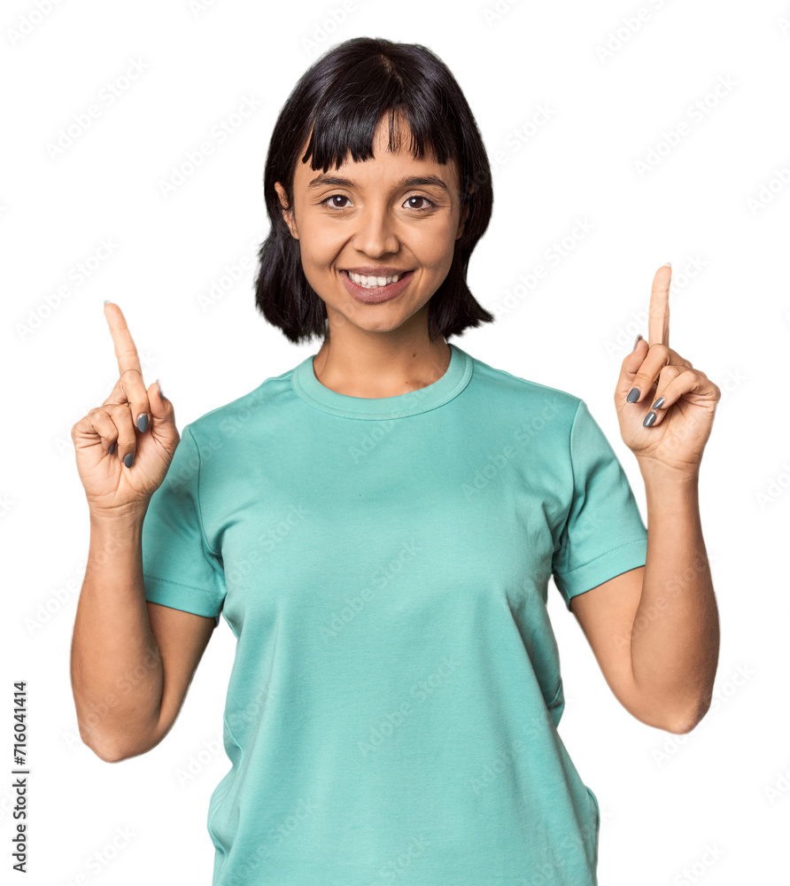 Young Hispanic woman with short black hair in studio indicates with both fore fingers up showing a blank space. Young Hispanic woman with short black hair in studio indicates with both fore fingers up showing a blank space.