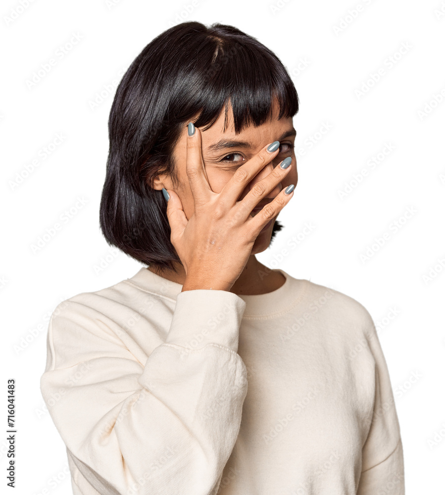 Young Hispanic woman with short black hair in studio blink at the camera through fingers, embarrassed covering face. Young Hispanic woman with short black hair in studio blink at the camera through fingers, embarrassed covering face.