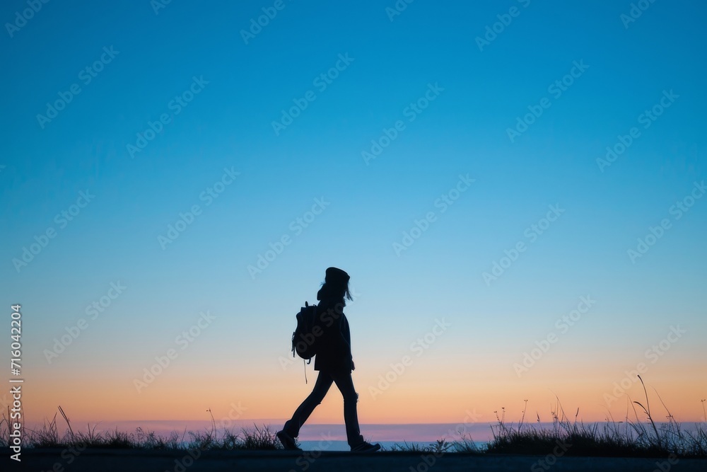 Against the winter horizon, a solitary figure treks through the sandy beach, their silhouette backlit by the warm glow of the sunset, carrying a heavy backpack and dressed for the outdoors under the 