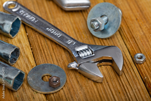 Adjustable wrench with bolts and melallic tools on wooden surface photo