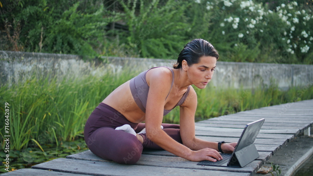 Yoga lady typing tablet sitting wooden bench. Tanned woman turning online lesson