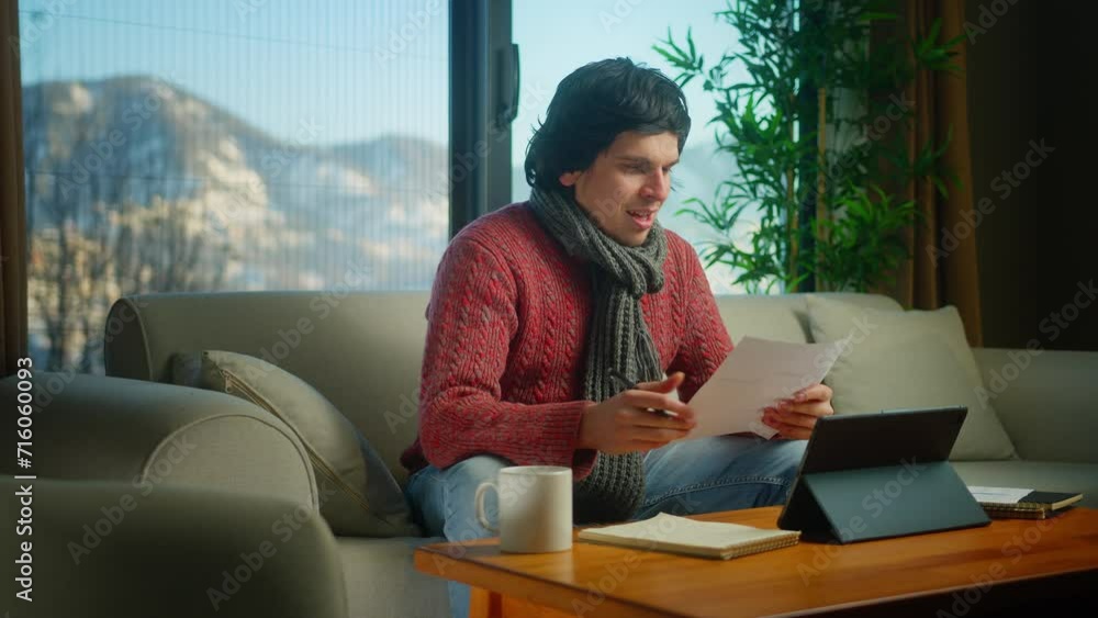 Young college student wear scarf sit on sofa doing research, homework with tablet device, taking notes. Man peaceful studying at home Young college student wear scarf sit on sofa doing research, homework with tablet device, taking notes. Man peaceful studying at home