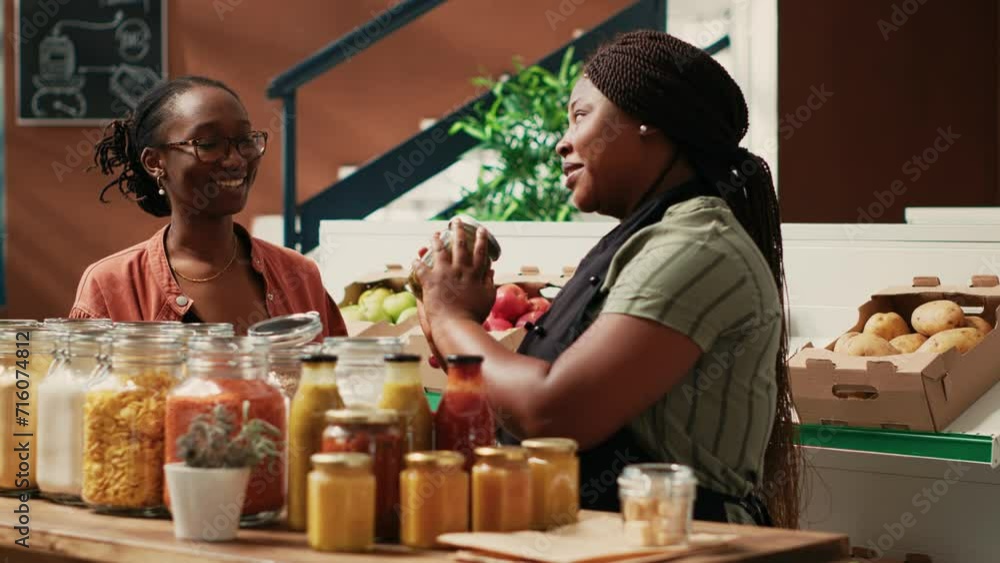 Merchant offering food sample to customer at farmers market, proving authentic natural taste of products before buying. African american business owner providing great service for shopper.