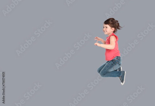 Cute girl jumping on grey background, space for text