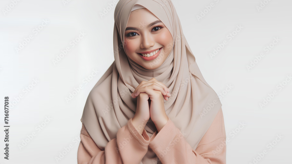 an Asian woman wearing a hijab poses with clasped hands with a happy smiling facial expression an Asian woman wearing a hijab poses with clasped hands with a happy smiling facial expression