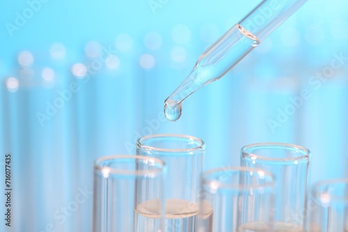 Laboratory analysis. Dripping liquid from pipette into glass test tube on light blue background, closeup and space for text