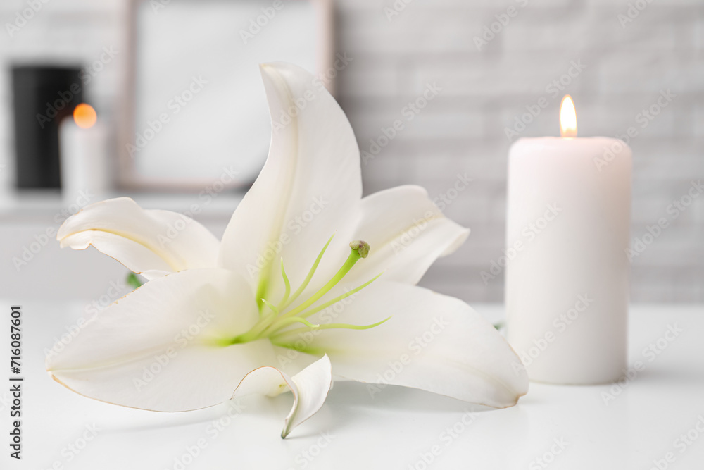 Burning candle and beautiful lily flower on light table in room, closeup
