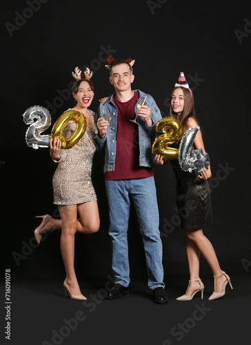 Young friends with champagne and figure 2024 on dark background. New Year celebration