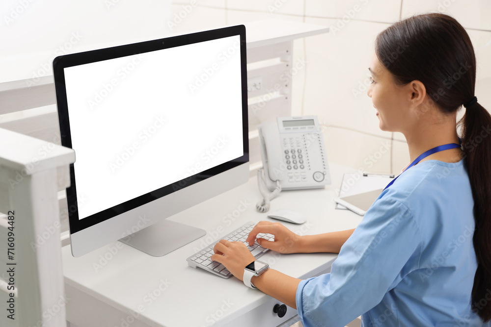 Female Asian medical intern working with computer at reception in clinic Female Asian medical intern working with computer at reception in clinic
