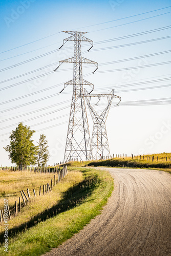 Transmission towers standing tall with power lines next to a gravel road overlooking the Alberta prairies in Rocky View County Canada.