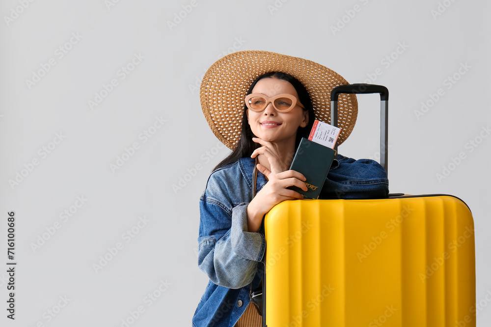Beautiful young woman in stylish hat with passport, ticket and suitcase on grey background Beautiful young woman in stylish hat with passport, ticket and suitcase on grey background