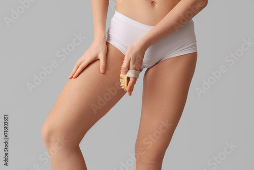 Beautiful young woman with cellulite problem and massage brush on grey background