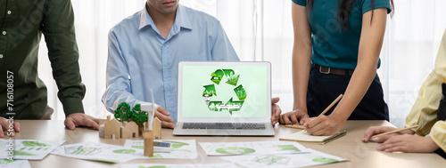Recycle sign displayed on green business laptop while business team presenting green design to customer. ESG environment social governance and Eco conservative concept. Closeup. Delineation
