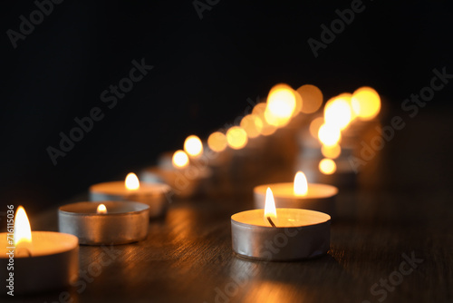 Burning candles on wooden shelf against black background, closeup. International Holocaust Remembrance Day photo