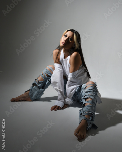 Full length portrait of brunette female asian model wearing casual clothes, double denim jean pants. Isolated on dark studio background with shadows