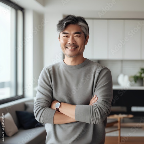 Portrait of handsome Asian man with crossed arms standing in modern apartment