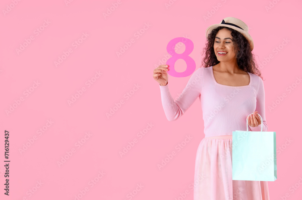 Fashionable African-American woman with figure 8 and shopping bag on pink background. International Women's Day celebration Fashionable African-American woman with figure 8 and shopping bag on pink background. International Women's Day celebration