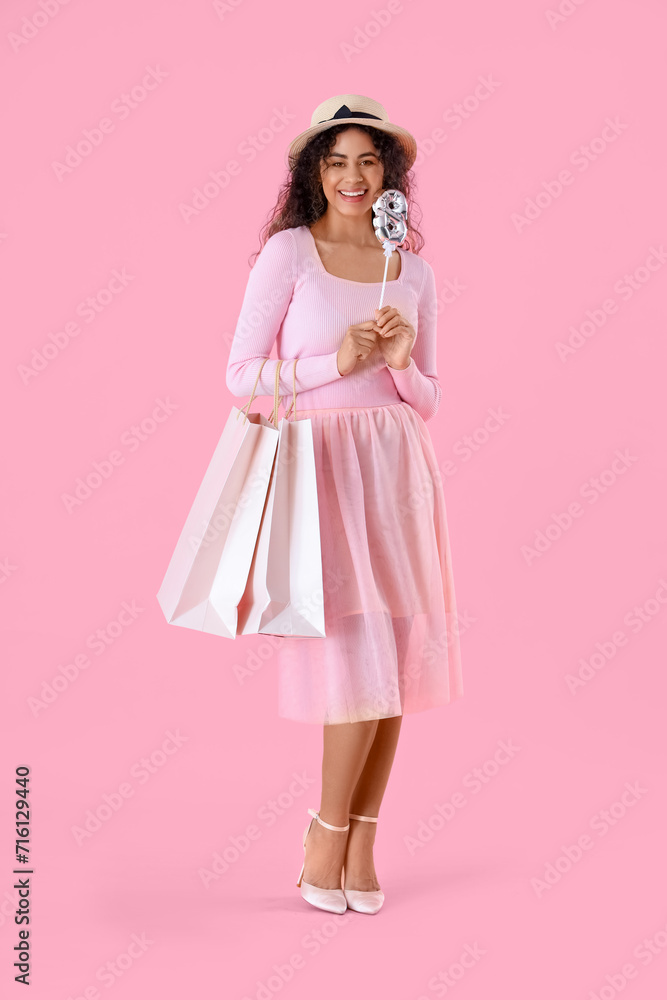 Fashionable African-American woman with balloon in shape of figure 8 and shopping bags on pink background. International Women's Day celebration Fashionable African-American woman with balloon in shape of figure 8 and shopping bags on pink background. International Women's Day celebration