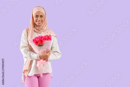 Muslim woman with bouquet of flowers for Ramadan on lilac background