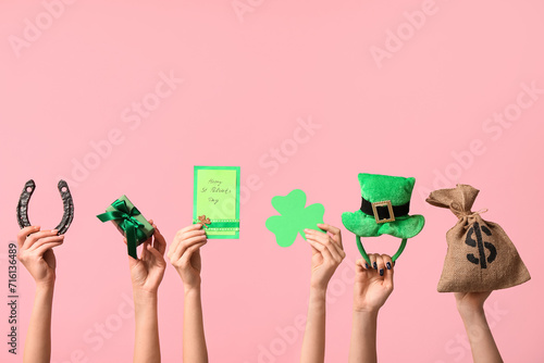 Female hands holding greeting card and party decor for St. Patrick's Day celebration on pink background