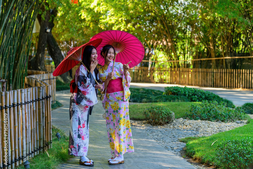 A young woman wearing a Japanese traditional kimono or yukata holding an umbrella is happy and cheerful in the park.