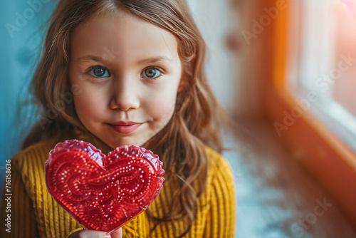 closeup little girl holding a big heart shaped lollipop