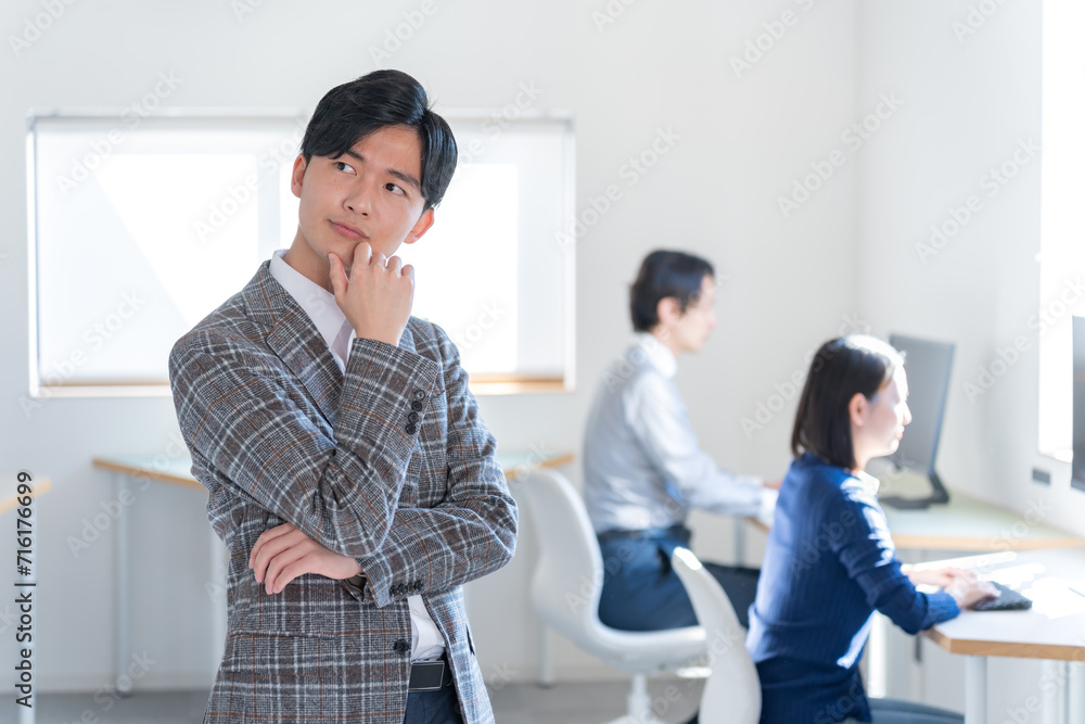 Naklejka premium オフィスで考えるジャケットを着た若い日本人男性